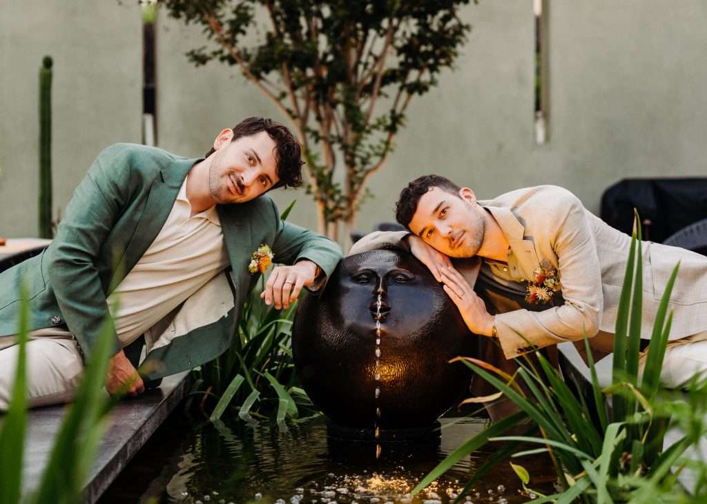 Two grooms leaning on fountain